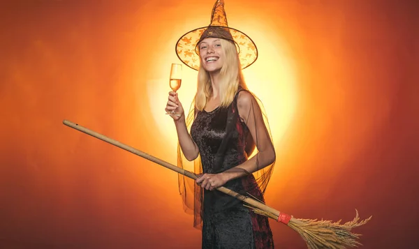 Surprised woman on witches hat and costume with broom - showing products. Vampire Halloween Woman portrait. Emotional young women on halloween party over red background. Looking camera
