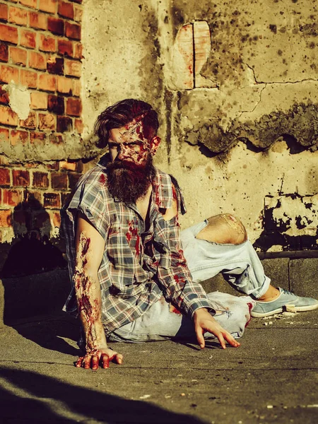 Zombie man sits on asphalt