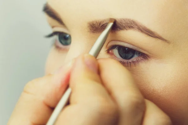 Mujer con ojos azules maquillándose las cejas —  Fotos de Stock