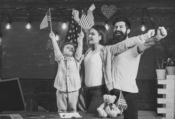 Kid with parents in classroom with usa flags, chalkboard on background. Parents teaching son american traditions playing. American cheerful family with son and usa flags. Patriotic education concept. — Stock Photo, Image