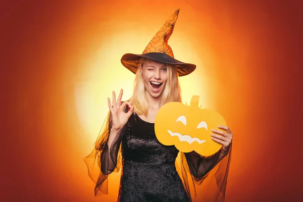 Femme surprise en chapeau de sorcières et costume sur fond rouge Halloween. Fête d'Halloween et concept de vacances. D'accord. . — Photo
