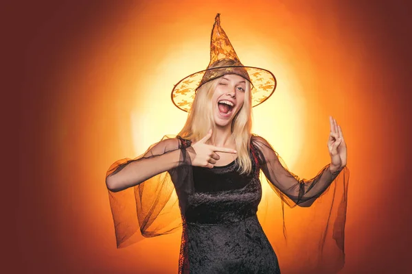 Mujer sorprendida con sombrero de brujas y traje sobre fondo rojo de Halloween. Hermosa joven sorprendida mujer en sombrero de brujas y traje señalando la mano - mostrando productos . — Foto de Stock