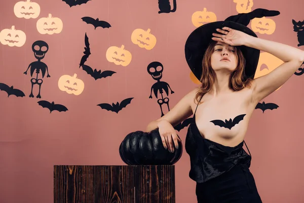 黒い帽子でハロウィンの魔女。女性がかぼちゃのポーズします。カボチャ頭のジャック ランタン。お菓子をくれないといたずらするよ。セクシーな魔女吸血鬼の概念。カボチャとポーズ美容女性. — ストック写真