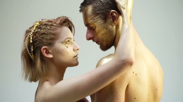 Ett ungt par i gyllene makeup berör varandra på en vit bakgrund. Begreppet erotica. Halloween party och fest koncept. — Stockvideo
