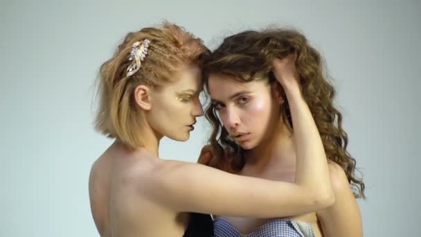 Dvě krásné dívky se zlatými make-up vzájemně dotýkají na bílém pozadí. Erotické koncept. Modelka ukazuje koncept luxusního. Vlasová kosmetika a kosmetika.