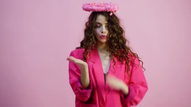 Curly flicka med tandställning i en rosa jacka gör luften pussar på en rosa bakgrund. Alla hjärtans dag firande. Rosa bakgrund. — Stockvideo