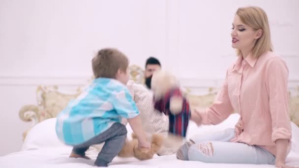 Mamma e figlio giocano con peluche a letto e papà leggono un libro sullo sfondo. Il concetto di famiglia felice. Famiglia felice in camera da letto . — Video Stock