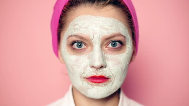Close-up of a girl with a mask on her face and a towel on her head with a wide-open eyes smiling. Beautiful girl with cosmetic mask on her face. Woman wearing face mask. Face care concept. — Stock Video