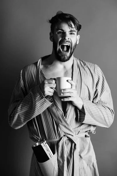 Angry man shouting with cup and magazine in robe pocket