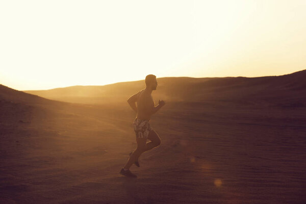 Healthy lifestyle and success. man runner or fit male athlete running in desert sand dune at mountain in sun ray at sunset, sunrise outdoor on white sky background. sprinting, sport and marathon