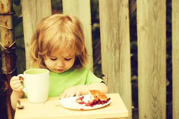 Маленький мальчик ест пирог возле деревянного забора — стоковое фото