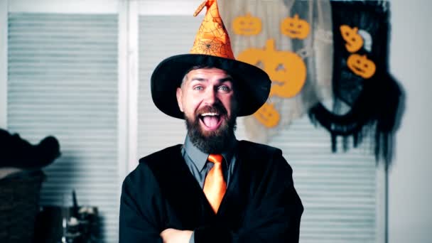 De bebaarde man in het witchs pak toont grimaces. Een bebaarde man in een oranje hoed toont grimaces op Halloween vakantie. Halloween feest en viering concept. — Stockvideo