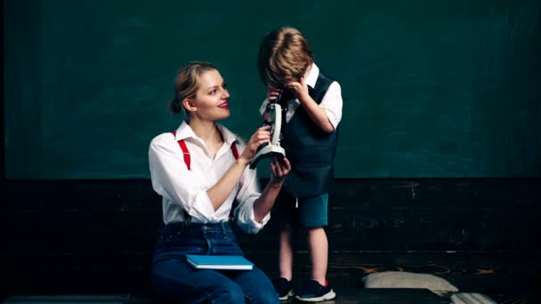 Una mujer con un niño pequeño mira el microscopio en el fondo de un tablero de pupilas verdes. Profesora en clase. Profesor y estudiante. Regreso a la escuela . — Vídeo de stock