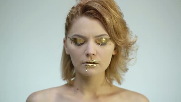 Nahaufnahme eines Mädchens mit goldenem Make-up, das vor weißem Hintergrund die Augen öffnet und schließt. Konzept des stylischen teuren Make-ups. — Stockvideo