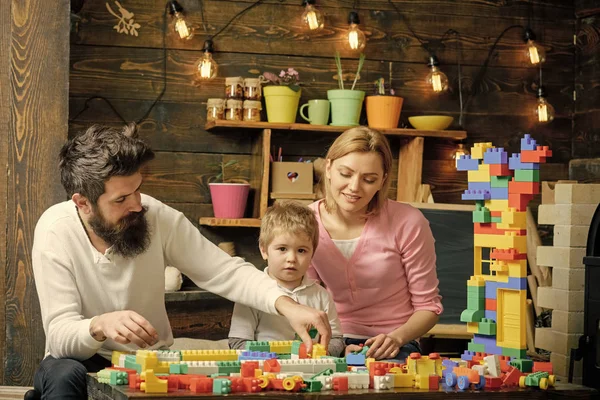 Familia en la cara ocupada pasar tiempo juntos en la sala de juegos. Concepto de juego educativo. Padre, madre e hijo lindo juegan con ladrillos constructores. Niño con los padres juegan con bloques de plástico, construir la construcción . — Foto de Stock