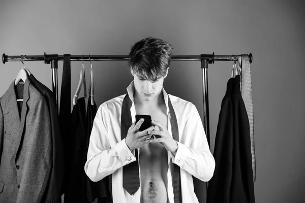 businessman with muscular torso at wardrobe hanger with phone