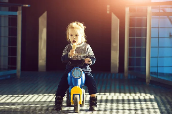 アイスクリームを食べて 遊んで 幼年期および教育コンセプトで道路日当たりの良い 屋外活動でのおもちゃのバイクに座っているかわいい少年の肖像画 — ストック写真