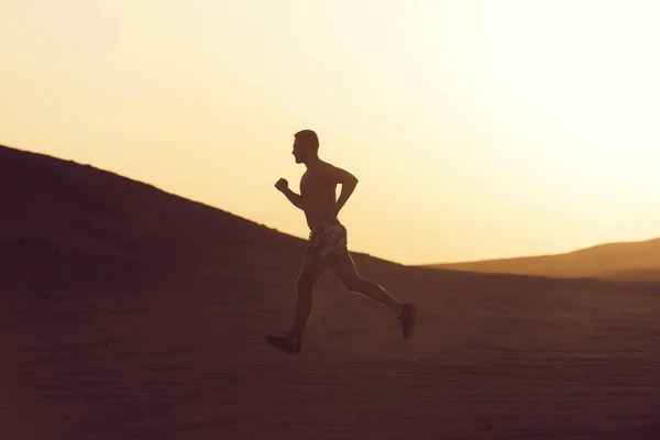 Man runner running in dune at sunset