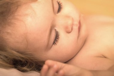 Bir güzel küçük uyuyan çocuk Childs'ın yüz sarı kıvırcık saçlı görünümünü closeup yuvarlak yanakları ve küçük parmak ile yatakta yatma, yatay resim kapalı kapalı gözler yalan
