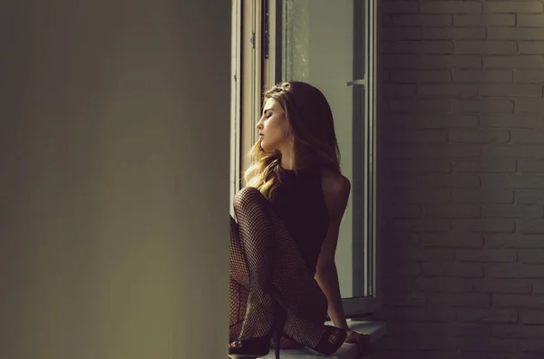 Docela sexy dívka sedící s nohama na okenním parapetu — Stock fotografie