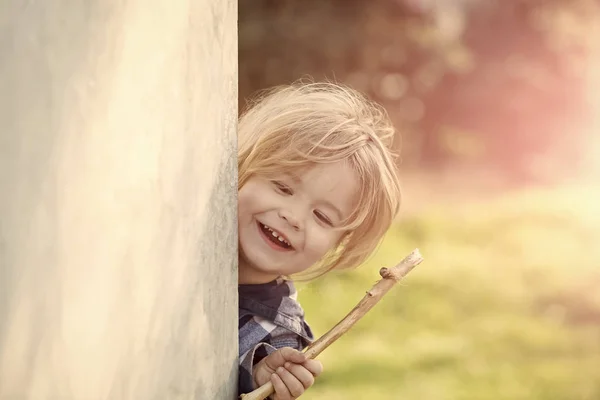 Enfant avec des cheveux blonds sourire avec bâton au coin du mur — Photo