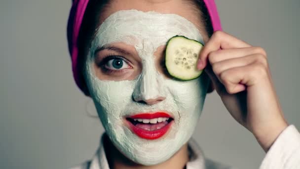 Gros plan d'une fille avec un masque facial et une serviette sur la tête qui ferme les yeux avec des concombres. Le concept de soin de la peau . — Video