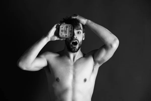 Shocked man covering eye with alarm clock on bearded face — Stock Photo, Image