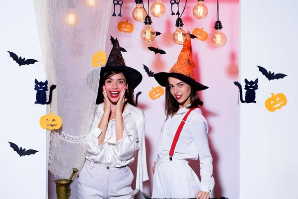 Emotional young women in halloween costumes on halloween party. Surprise. Halloween girls through hole in white wall. Best friends girls celebrates thanks giving day. Halloween copy space.