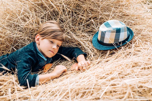 마을에서 가을 휴가를 보내는 귀여운 소년. 그 소년 은가을에 아이들의 옷을 광고한다. 건초더미에 모자쓴 쾌활 한 남자. 행복 한 어린 시절. — 스톡 사진