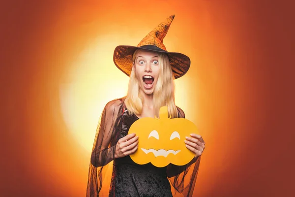 Mujer joven gótica feliz disfrazado de bruja de halloween con sombrero de pie y sonriendo sobre fondo blanco. Bruja de Halloween con calabaza . — Foto de Stock