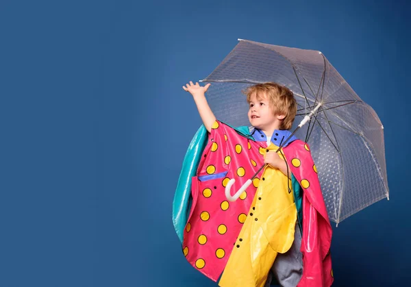 Niño alegre en impermeable con paraguas colorido. Lindo niño pequeño usando ropa de otoño en el día de lluvia de otoño. El niño se está preparando para el día soleado de otoño. Niño bajo la lluvia . — Foto de Stock