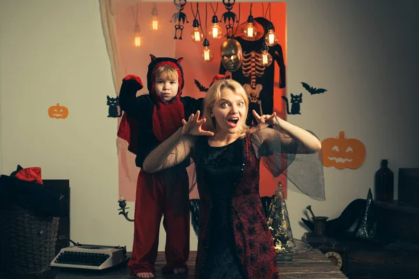 Madre vistiendo como bruja, hijo vistiendo como demonio. Niño disfrazado de diablo. Hermosa joven con un niño con calabazas. Sonrientes madre e hijo. Madre y su hijo niño jugando juntos . — Foto de Stock