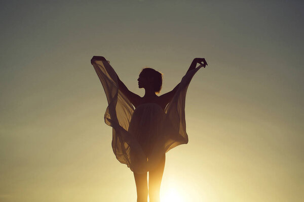 Silhouette of slim girl young woman female model dances in transparent windy dress on nature over beautiful sunset