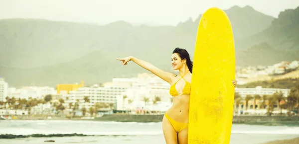 Surfista menina muito feliz com amarelo surfboard aponta dedo — Fotografia de Stock