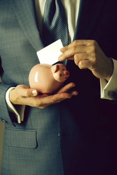 Male hands putting business card in piggy bank