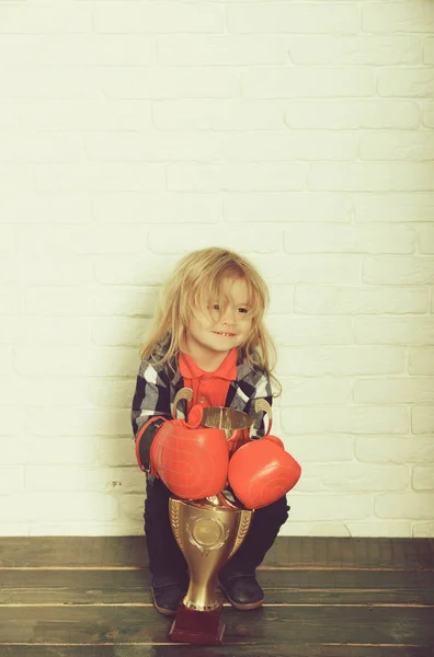 happy kid winner in boxing glove, boy boxer winning golden champion cup on white brick wall background