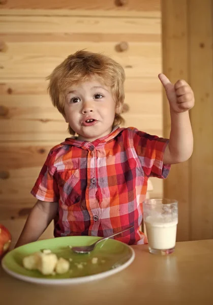 Kid or blonde happy boy eating at table.