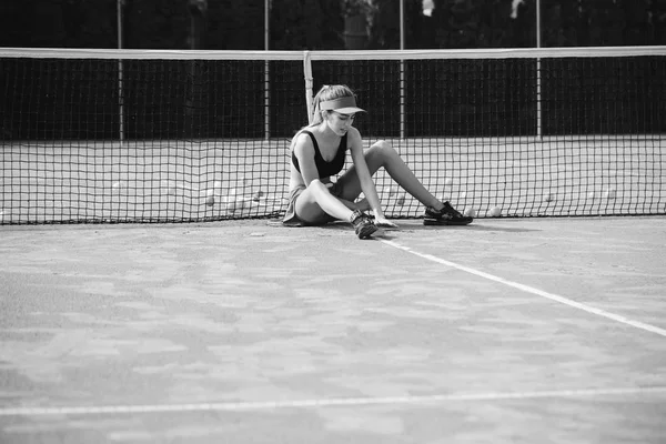 Woman sitting and relax on tennis court in cap — Stock Photo, Image