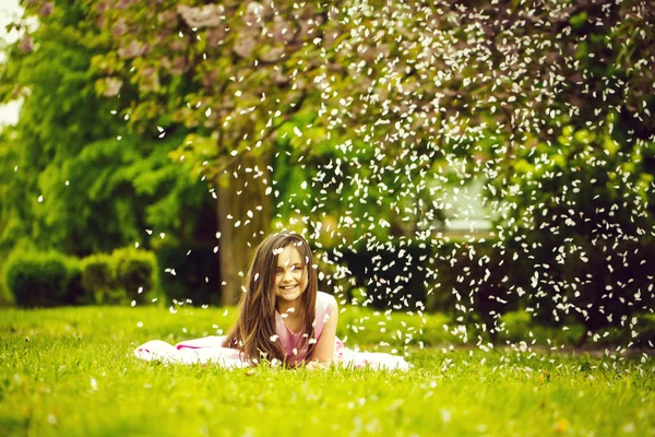 Little girl on green grass with petals — Stock Photo, Image