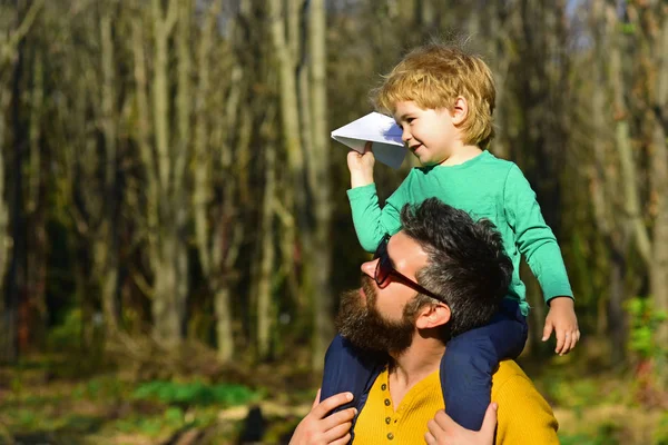 Volar es la vocación perfecta para un hombre que quiere sentirse como un niño. Hijo pequeño sueño de volar sobre el hombro de los padres. Niño y padre lanzan avión de papel en el parque — Foto de Stock