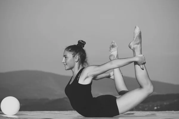 Woman gymnast with green ball on blue sky background