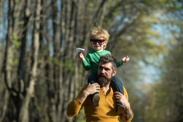 Niño jugando con avión de papel en el hombro del padre en el parque. Padre e hijo jugando juntos al aire libre. Es hora de volar — Foto de Stock