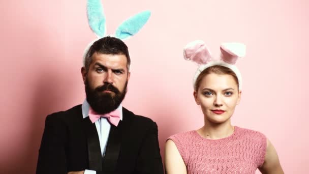 Bearded man and blond woman raising eyebrows on a pink background with ears on their heads. Concept of fashionable hare. Man and woman with hare ears on a pink background.