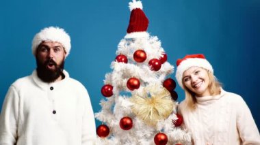 Genç çift mavi arka plan Noel ağacına yakın duran palyaçoluk yapar. Sakallı adam ve sarışın bir kadın tarafından ağaç stand ve üzerinde mavi arka plan gülümsemek. Yeni yıl kavramı.