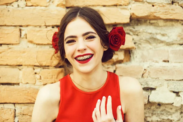 レンガ壁の背景上の髪でローズと明るい赤いドレスでファッショナブルな幸せな女 — ストック写真