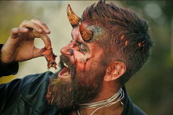 Halloween satan man with horns on head eating bloody meat — Stock Photo, Image