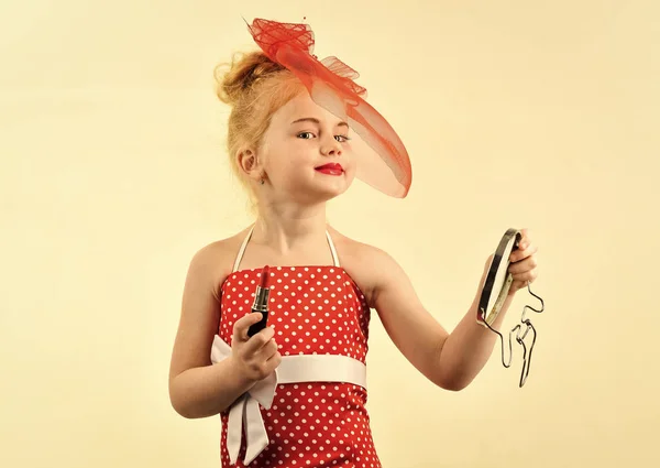 Look rétro maquillage et coiffeur. Mode fille rétro avec cosmétiques, beauté. Mode et beauté, style pin-up, enfance. Enfant fille en robe élégante, maquillage. Petite fille tenir rouge à lèvres et miroir . — Photo