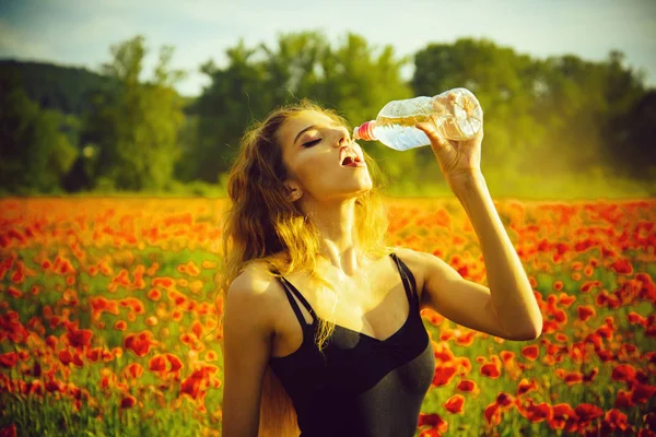 Женщина в поле маковых семян пить воду из бутылки — стоковое фото