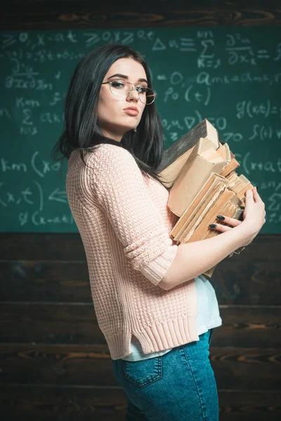 Vista lateral morena estudiante femenina con dos montones de libros. Elegante chica universitaria en gafas con cárdigan rosa va a la biblioteca — Foto de Stock