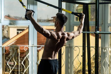 Spor ve spor salonu konsept. Adam çıplak gövde ve geri içinde jimnastik salonu kas eğitim, trx tadını çıkarın. Gövde, sporcu, atlet, kas maço mu egzersiz trx döngüler ile pencere arka plan üzerinde olan adam